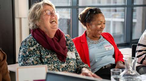 Twee lachende dames aan gesprekstafel | Krachtig ouder worden
