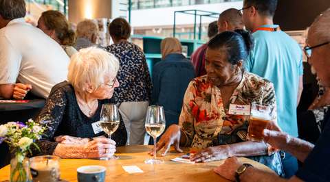 Twee dames in gesprek aan tafel tijdens borrel | Krachtig ouder worden